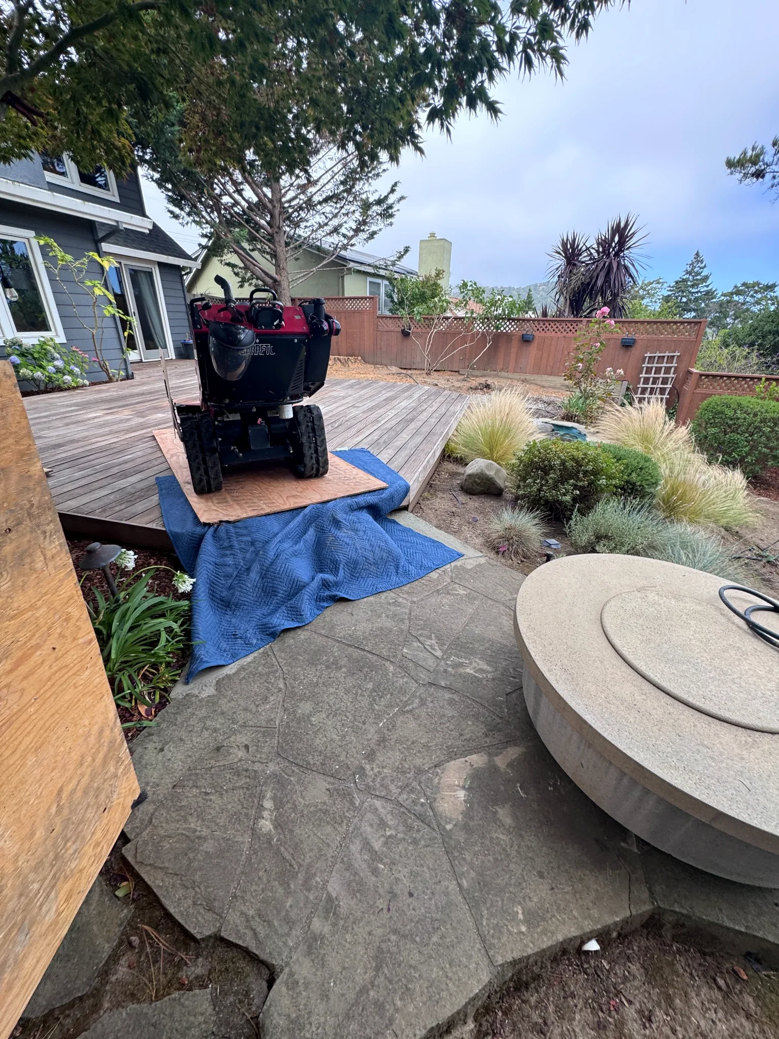 Plywood and moving blankets protecting hardscape beneath a stump grinder